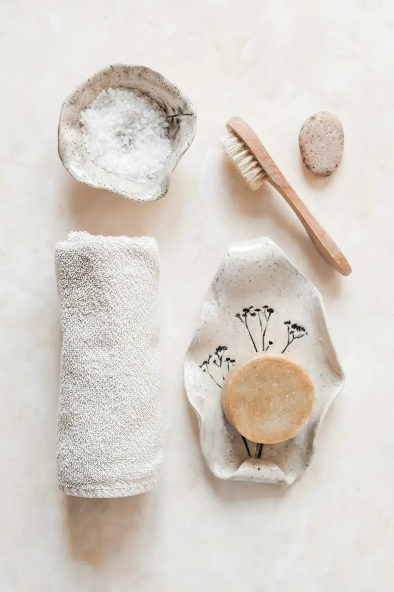 A bath ritual still life with a folded towel, a wooden brush, bath salts and a bar of soap