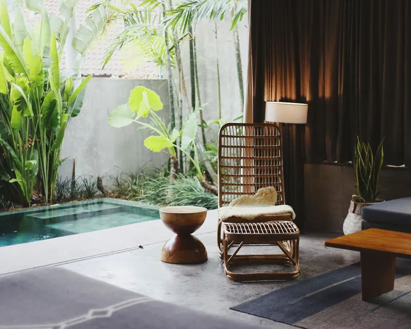 A calm, sunlit room with a rattan chair, a stool and green plants